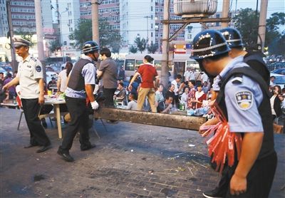 6月13日晚8點，朝陽路和青年路交叉口西側，一次聯(lián)合執(zhí)法行動中，輔警與協(xié)管抬走商戶的燒烤用具。新京報記者 尹亞飛 攝