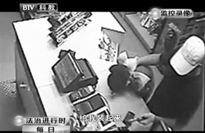 戴帽男子一手掐住加油站營業(yè)員，一手持發(fā)令槍指向另一營業(yè)員，要求“把錢給我裝起來”。