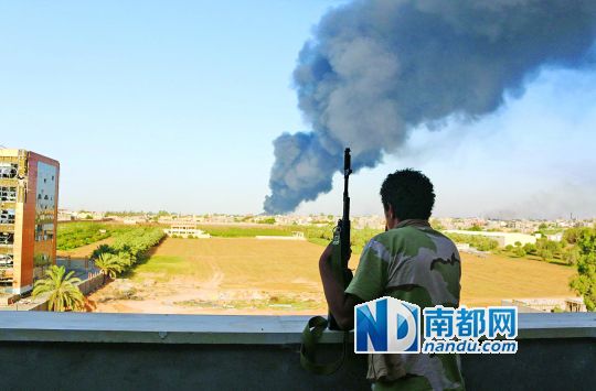 2日，利比亞首都的黎波里，一民兵武裝成員眺望被火箭彈擊中的儲油罐冒出濃煙。