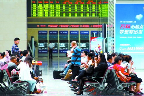 候車大廳溫度很高，一名乘客一手扇風(fēng)、一手擦汗
