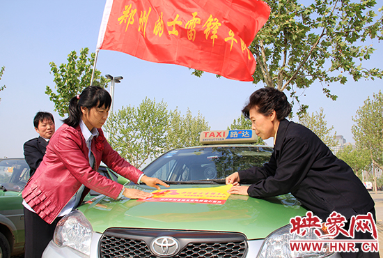 　　授旗結(jié)束后，首都的士雷鋒車隊(duì)王鳳進(jìn)隊(duì)長(zhǎng)（右）與鄭州的的哥的姐在車身上貼上標(biāo)識(shí)。
