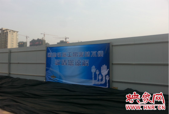 道路南側(cè)圍起了白色的圍擋，墻上標示著“因地鐵施工帶來的不便敬請您諒解”的提示牌。
