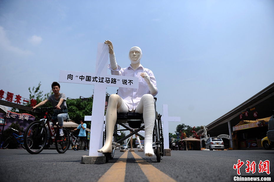 4月16日，重慶市洋人街上擺放著兩個受了傷的塑料人像“模特”，旁邊十字架上寫著向“中國式過馬路”說不