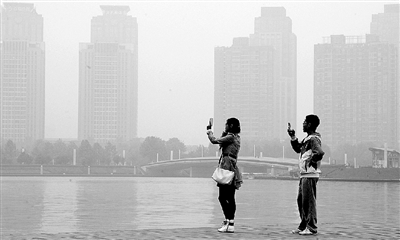 29日中午，鄭東新區(qū)如意湖畔，兩個(gè)年輕人拍攝霧霾中的景色。 鄭州晚報(bào)記者 馬健 圖