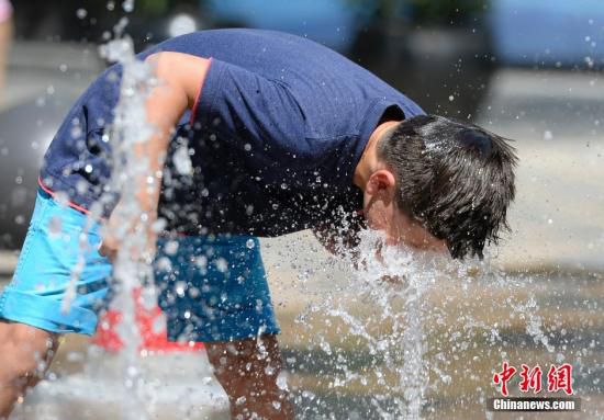 5月29日，一名小孩將頭伸向北京街頭的噴泉以降溫祛暑。