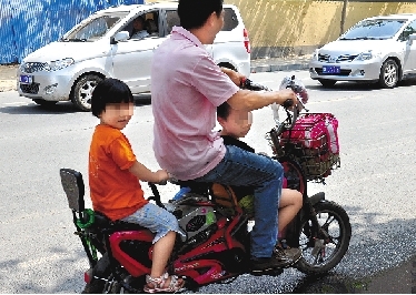 周先生騎著一輛低矮的電動車帶著一對兒女，很不安全。