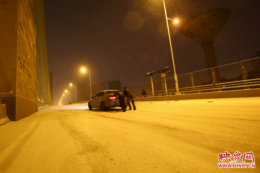 雪天路滑，汽車上橋打滑，兩名“推車人”幫助一輛私家車上坡。