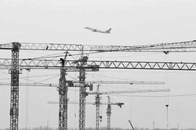 空中是起飛的飛機(jī)，下面是T2航站樓工地上林立的塔吊