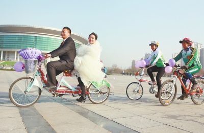 氣球和鮮花裝點(diǎn)的雙人自行車，新郎郝幸福載著美麗新娘回家。