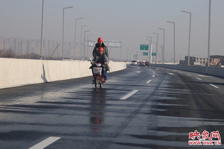 兩名工人騎車經(jīng)過灑水養(yǎng)護(hù)路面。