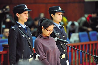 被告人盧梅低著頭，站在朝陽法院刑事審判庭的被告席上。